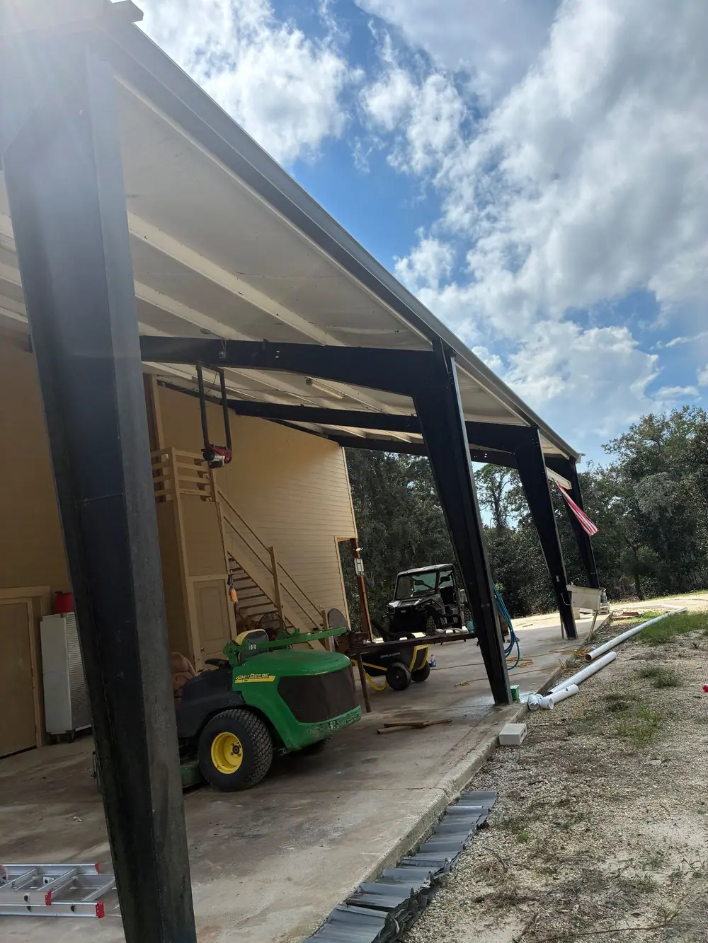 Gutter along the eave of a steel-frame carport, with downspout pipe laid out on the ground