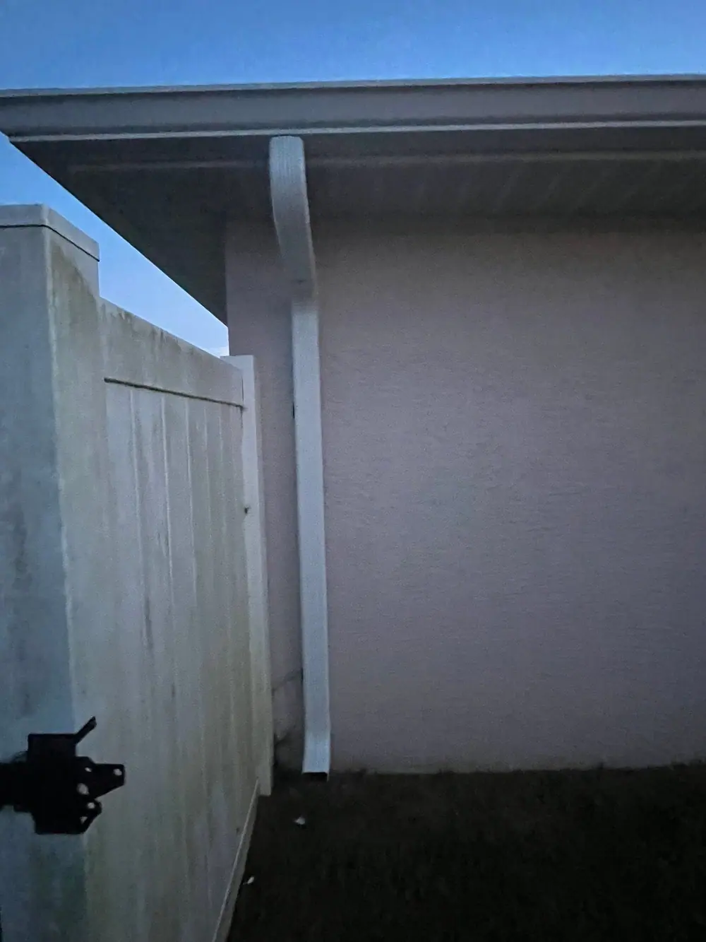White downspout running down a wall beside a privacy fence