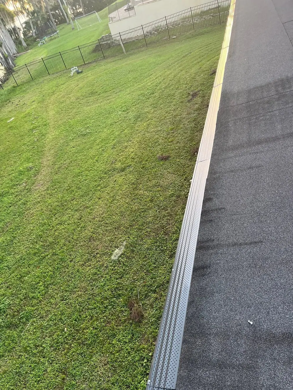 Gutter guard running along a roof edge above a green lawn