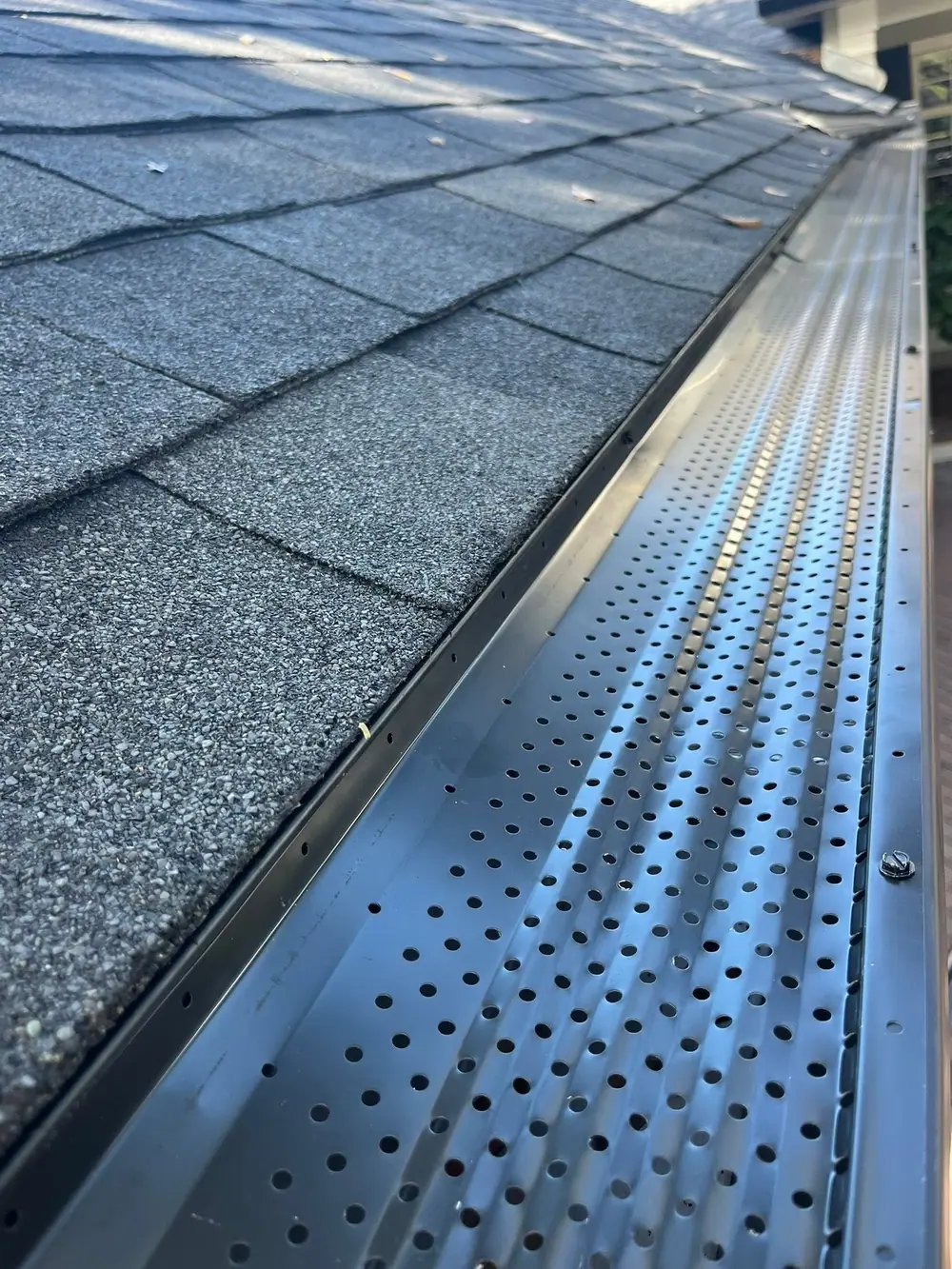 Perforated metal gutter guard installed over a gutter on a shingle roof