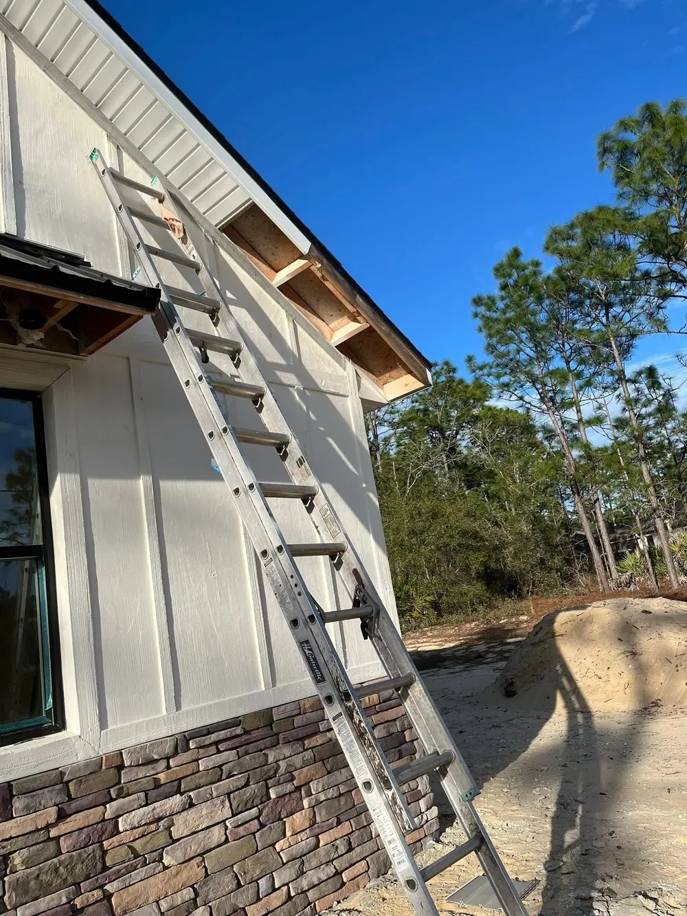 Ladder against a board-and-batten home with a stone base during a gutter install