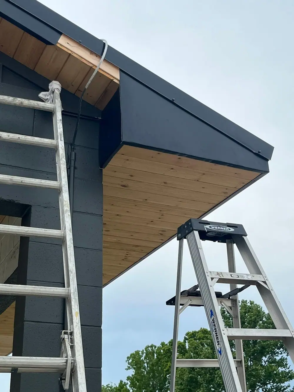 Dark home with wood-look soffit and new gutter, ladders set against the wall
