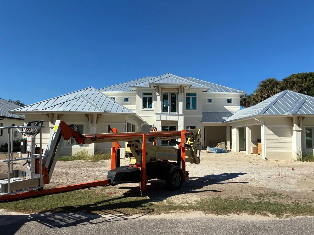 New construction home with a standing-seam metal roof and white gutters, boom lift in the drive