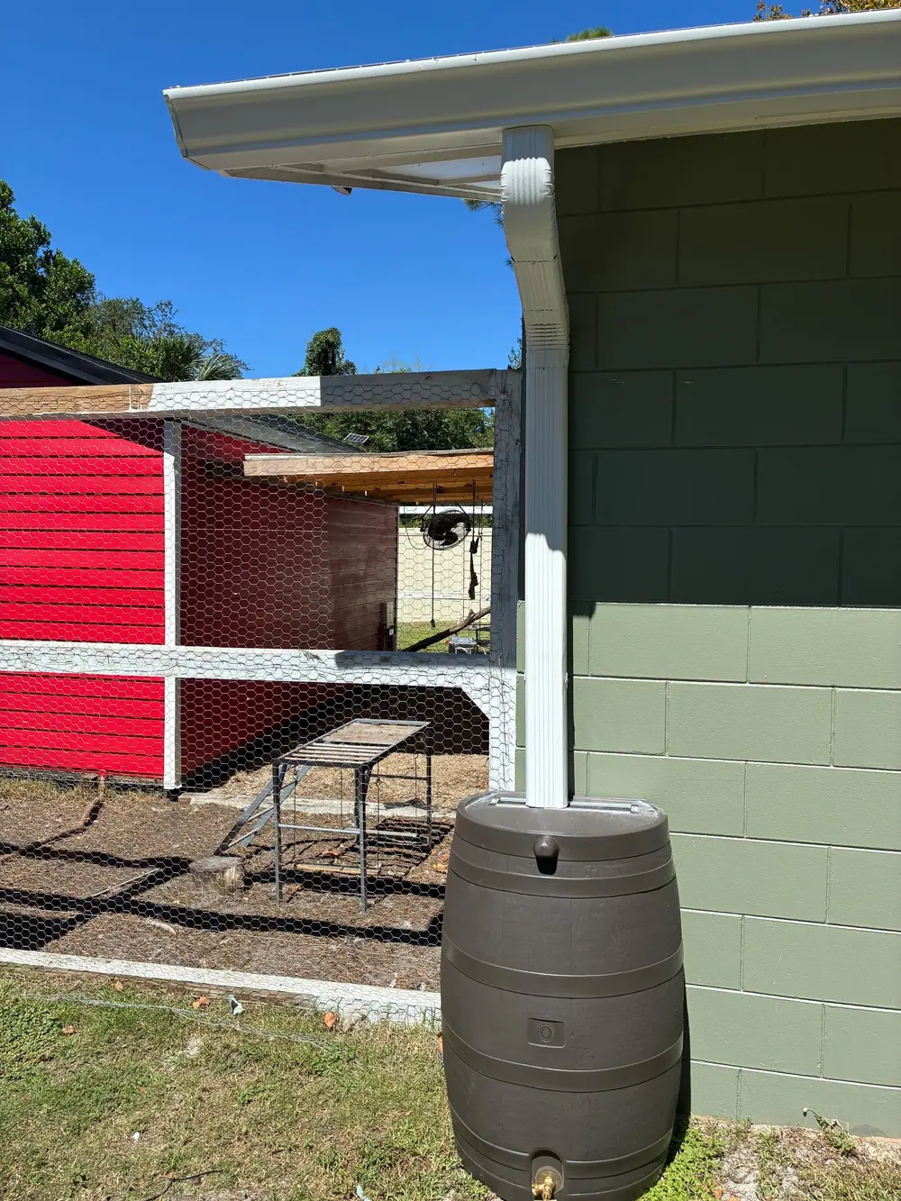 White gutter and downspout feeding a rain barrel beside a block wall