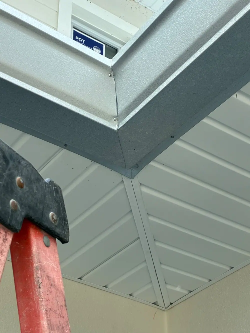 Mitered silver gutter corner over new vented soffit, seen from the ladder