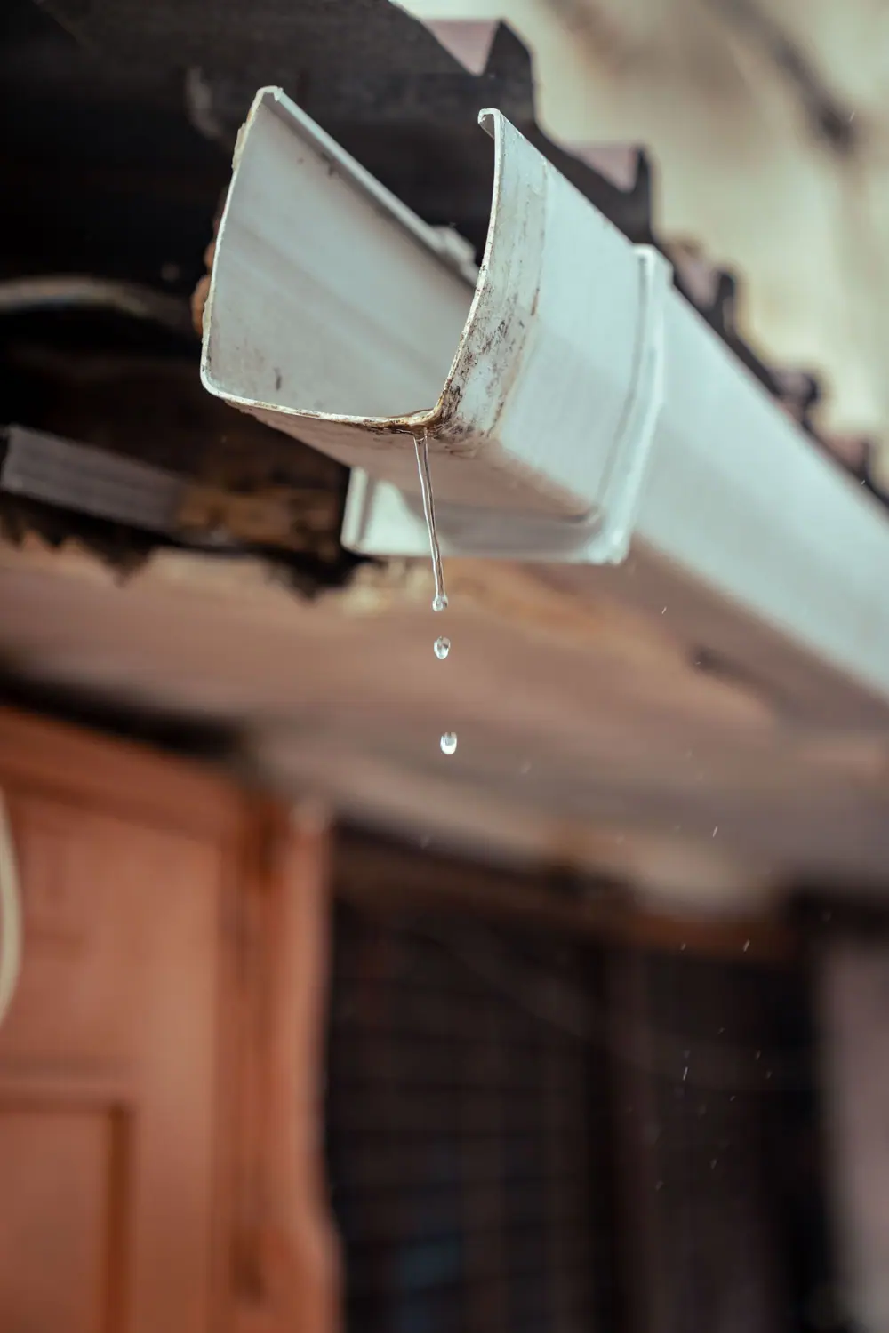 Water dripping from the end of a white gutter after rain (stock photo)
