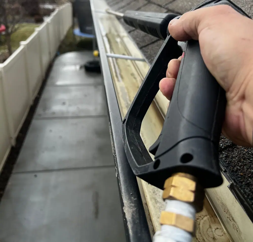 Pressure washer wand flushing debris out of a gutter on a shingle roof (stock photo)
