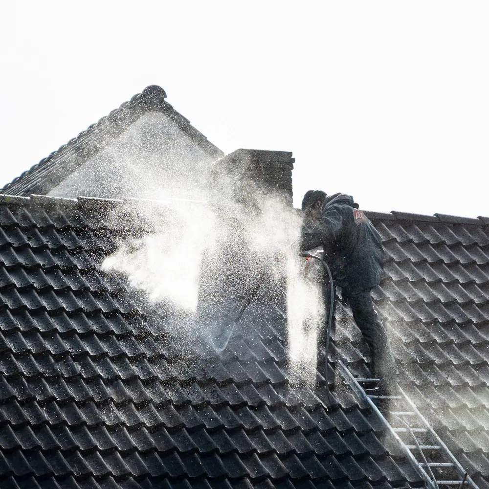 Worker washing a tile roof from a ladder in a cloud of spray (stock photo)