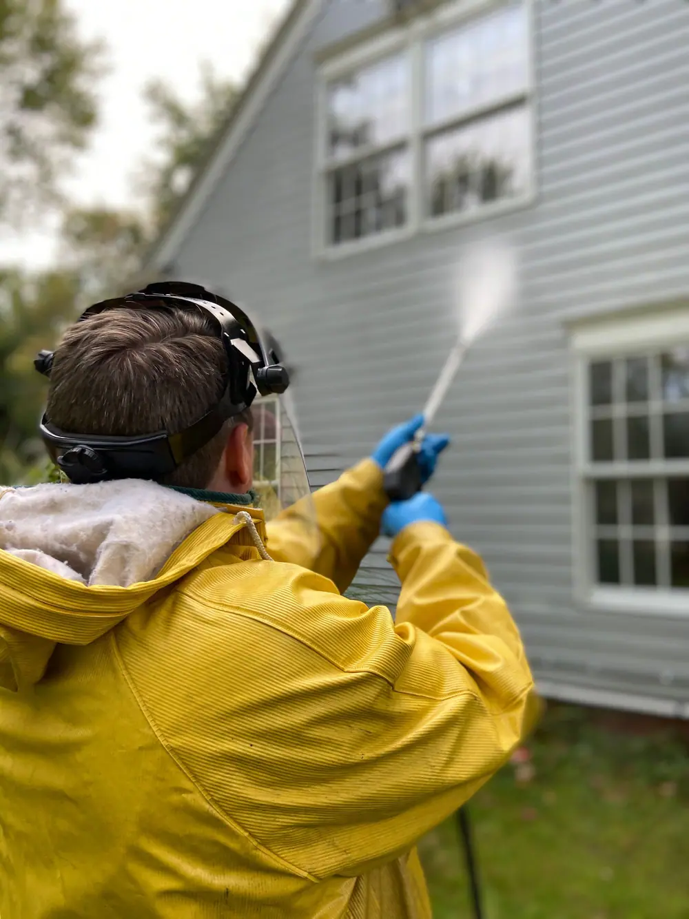 Person in a rain jacket pressure washing house siding (stock photo)